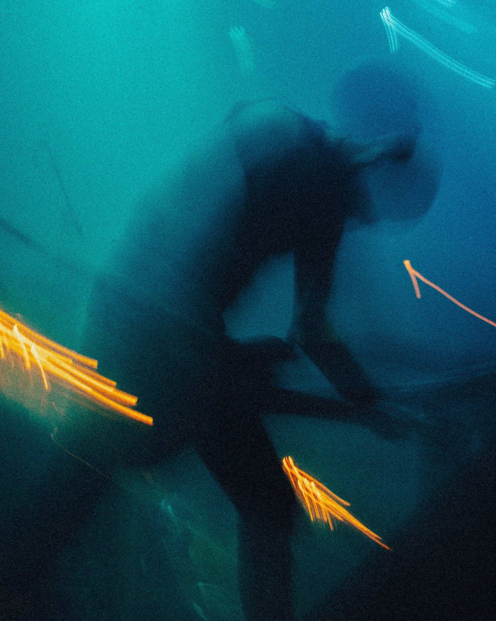Blurred silhouette bending forward with arm raised near face, set against teal light with two clusters of orange spark trails streaking diagonally in the foreground.