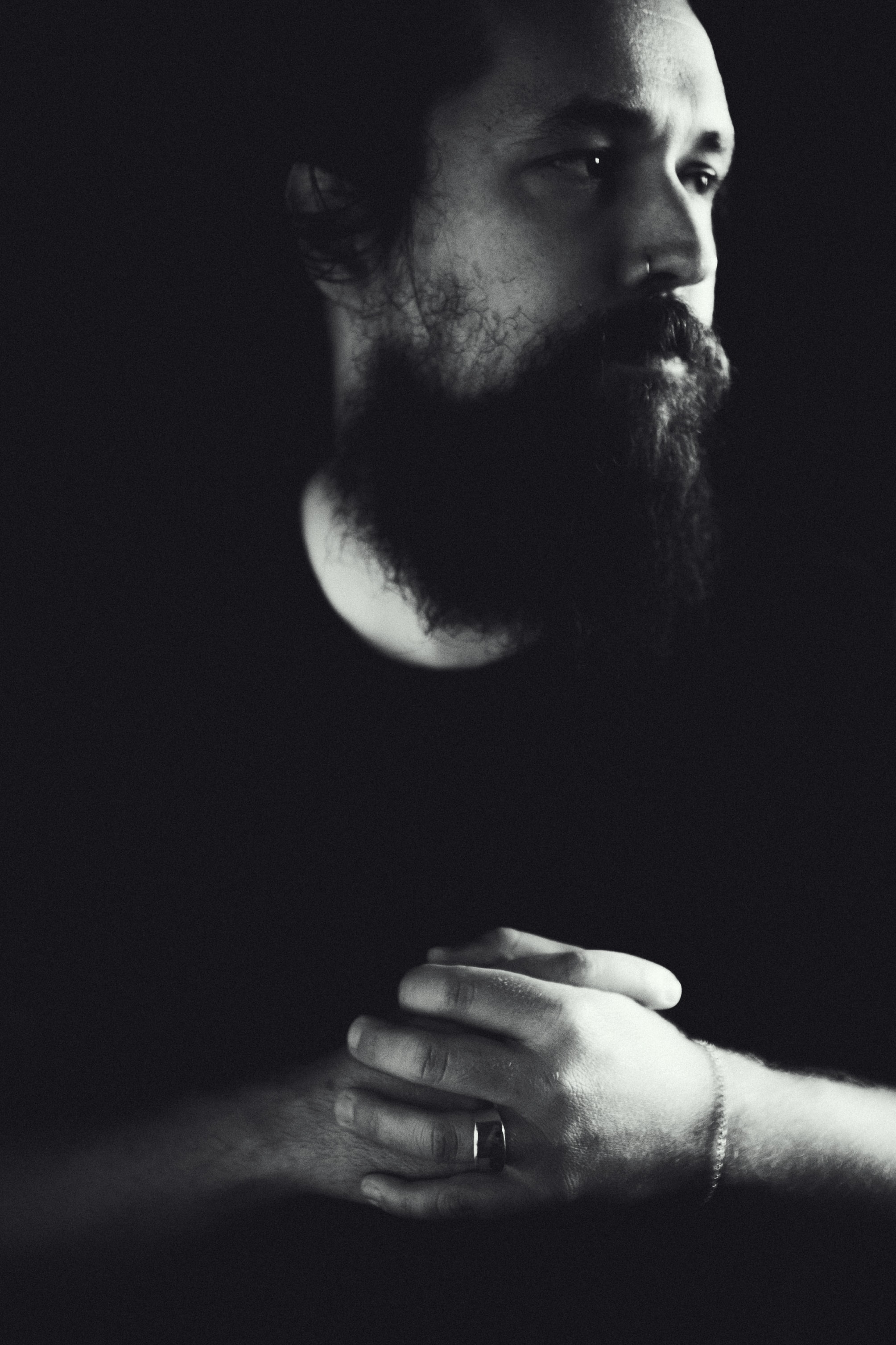 Black-and-white portrait of Zach K. Johnson in profile, hands clasped in front of him, lit in dramatic low-key shadow against a dark background